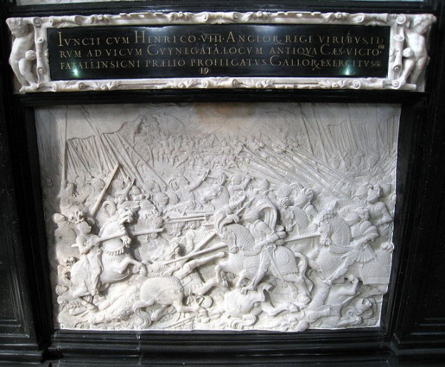 Weißer Marmorstein mit schwarzem Rand an einem Gebäude, der eine Schlachtenszene mit Schwert- und Schildträgern zeigt, umgeben von Zuschauern.