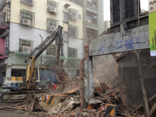 Ein Bagger auf einer Straße mit Bannern, Gebäude mit Fenstern und dem Himmel im Hintergrund.