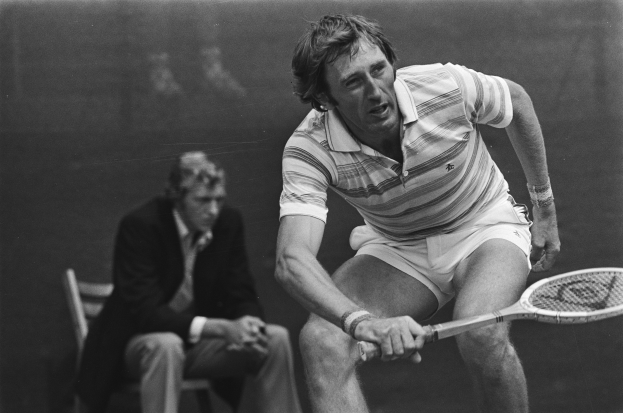 Mann schwingt Tennisracket gegen einen Ball, mit einer weiteren Person im Hintergrund, dargestellt in Schwarz-Wei├č.