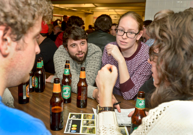 Mehrere Personen auf beiden Seiten eines Tisches mit Bierflaschen in einer Bar.
