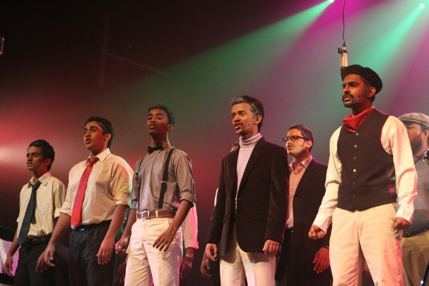 Eine Gruppe von Männern auf einer Bühne, die ein Drama mit grünen Scheinwerfern im Hintergrund spielen.