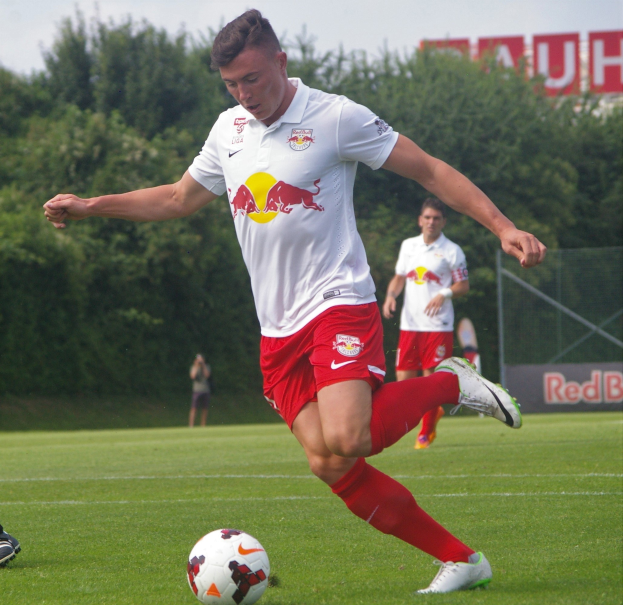 Ein professioneller Fußballspieler tritt einen Fußball auf einem grünen Feld, auf dem "RB Leipzig" zu sehen ist.
