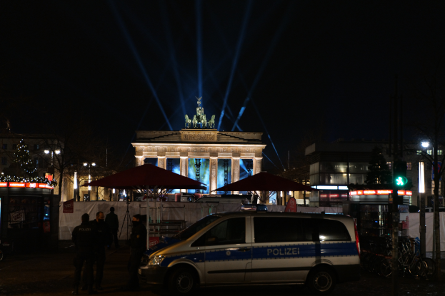 Ein Polizeiwagen steht nachts vor dem Reichstagsgebäude in Berlin, umgeben von ein paar Menschen und diversen Gegenständen, die in der Gegend verstreut sind.