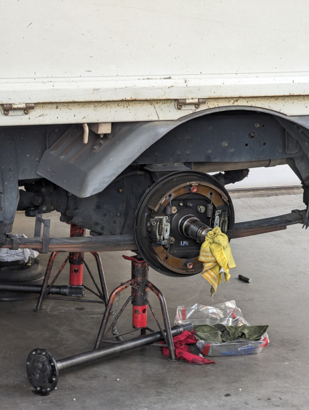 Ein gelber, tuchbedeckter Lkw in einer Garage mit Werkzeugen und Gegenständen, die vor ihm auf dem Boden verstreut sind.