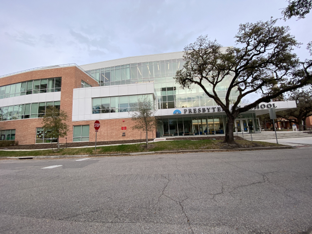Presbyte Mittelschule, ein großes Gebäude mit zahlreichen Fenstern, umgeben von Bäumen, Gras, Schildern, Pfählen und einer Straße, mit einem bewölkten Himmel im Hintergrund.