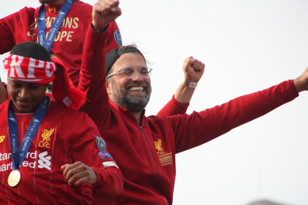 Liverpool-Trainer Jürgen Klopp feiert mit seinen Spielern nach dem Gewinn der UEFA Champions League, umgeben von zwei medaillen tragenden Personen und dem Himmel im Hintergrund.