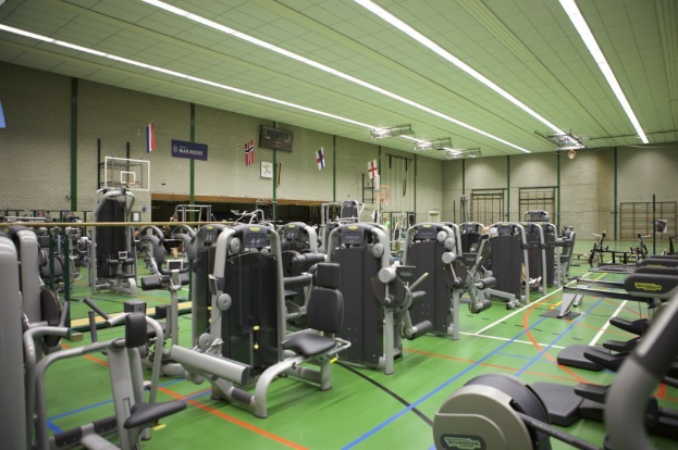 Ein geräumiges Fitnessstudio mit verschiedenen Trainingsgeräten, eine Wand mit Flaggen und Deckenleuchten.