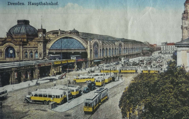 Schwarz-weiß-Postkarte des Dresdner Hauptbahnhof in Deutschland, die eine belebte Straße mit Fahrzeugen, Fußgängern, Bäumen, Gebäuden und einem bewölkten Himmel zeigt.