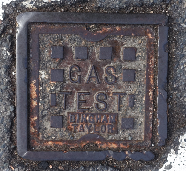 Ein Metall-Schachdeckel auf dem Boden mit der Aufschrift "Gas Test".