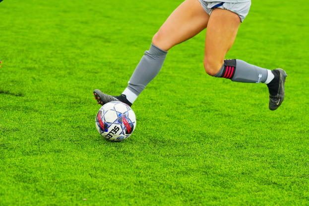 Eine Frau in einem Sportoutfit kickt einen Fußball auf einem saftigen grünen Feld.
