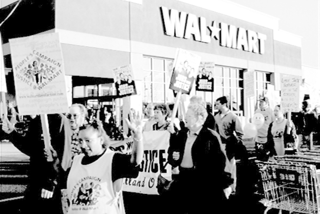 Ein Schwarz-Weiß-Bild von protestierenden Menschen mit Plakaten und einem Einkaufszentrum im Hintergrund.