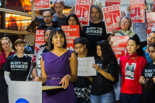 Eine Black-Lives-Matter-Aktivistin spricht vor einem Publikum mit Mikrofon, das Plakate hält, mit Lichtern und anderen Gegenständen im Hintergrund.