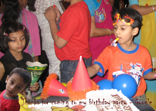 Kinder vor einem Tisch mit einem Kuchen, Luftballons und Mützen, während andere Menschen im Hintergrund zu sehen sind.