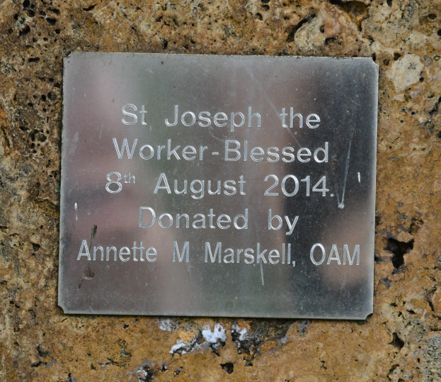 Eine Steinmauer mit einer Metalltafel, auf der "St. Josef der Arbeiter-Gesegnet 8. August 2014" steht.