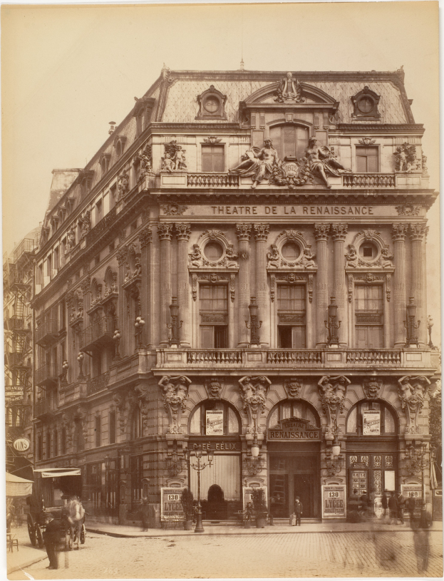 Ein altes Foto des Théâtre de la Renaissance in Paris, Frankreich, das ein Gebäude mit Fenstern, Säulen, Bögen und Skulpturen an der Fassade zeigt, mit einigen Menschen und Fahrzeugen auf der Straße davor und dem Himmel im Hintergrund.