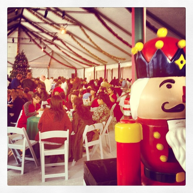 Eine Gruppe von Menschen feiert Weihnachten in einer Hütte, mit einem geschmückten Baum, weißen Stühlen, einem roten Spielzeug-Wachmann und einer schwarzen Krone.