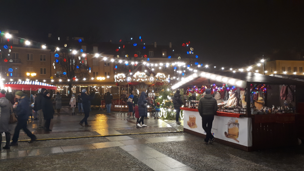 Ein lebendiger Weihnachtsmarkt in einer Stadt bei Nacht, mit Menschen, die herumlaufen, Ständen, die mit Lichtern und Dekorationen geschmückt sind, Gebäuden mit Fenstern, Bäumen und einem Himmel, der mit festlichen Lichtern erleuchtet ist.