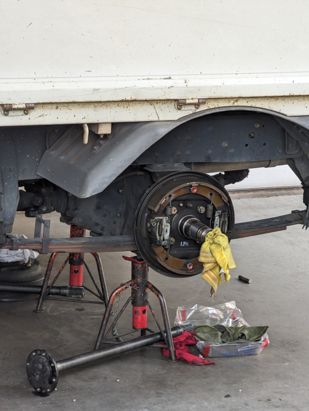 Ein Lkw in einer Garage geparkt, mit einem gelben Tuch darüber, umgeben von verschiedenen Werkzeugen und Gegenständen auf dem Boden.